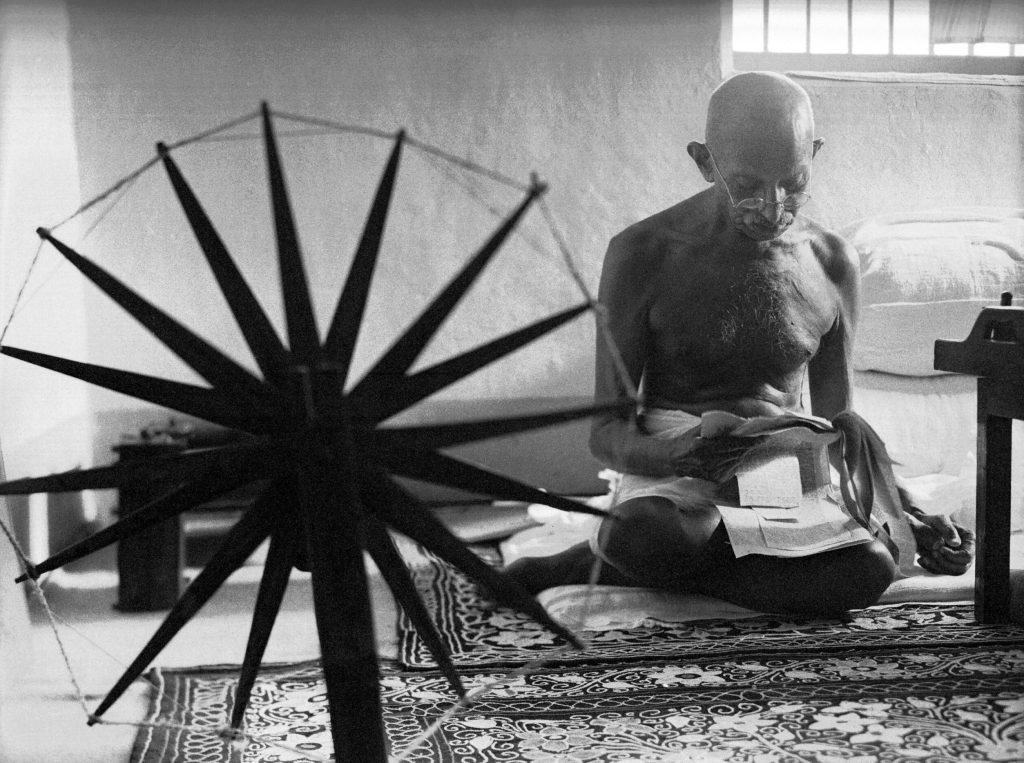 Indian leader Mohandas Gandhi reading next to a spinning wheel at home.